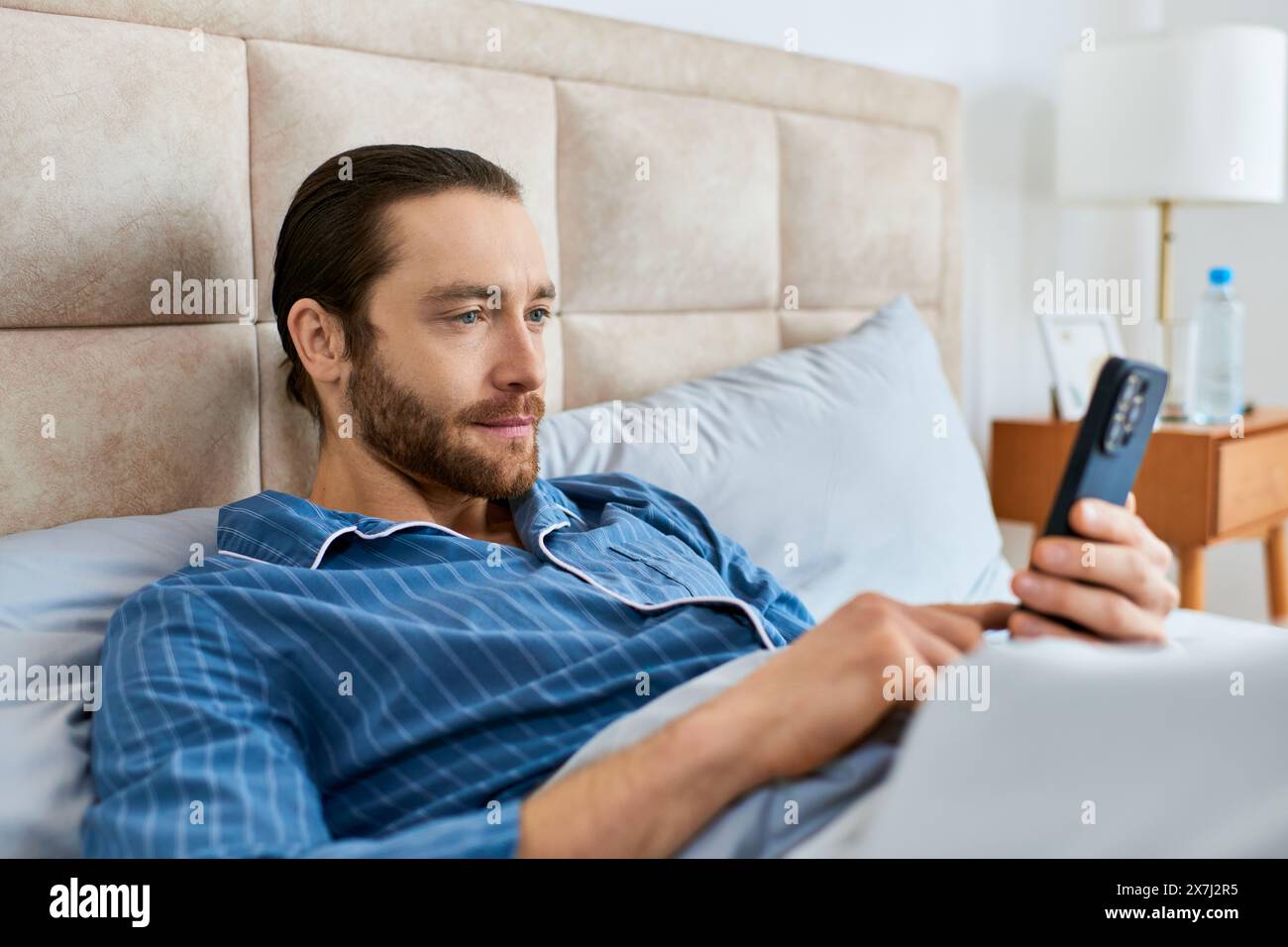 Man peacefully rests in bed, holding phone. Stock Photo