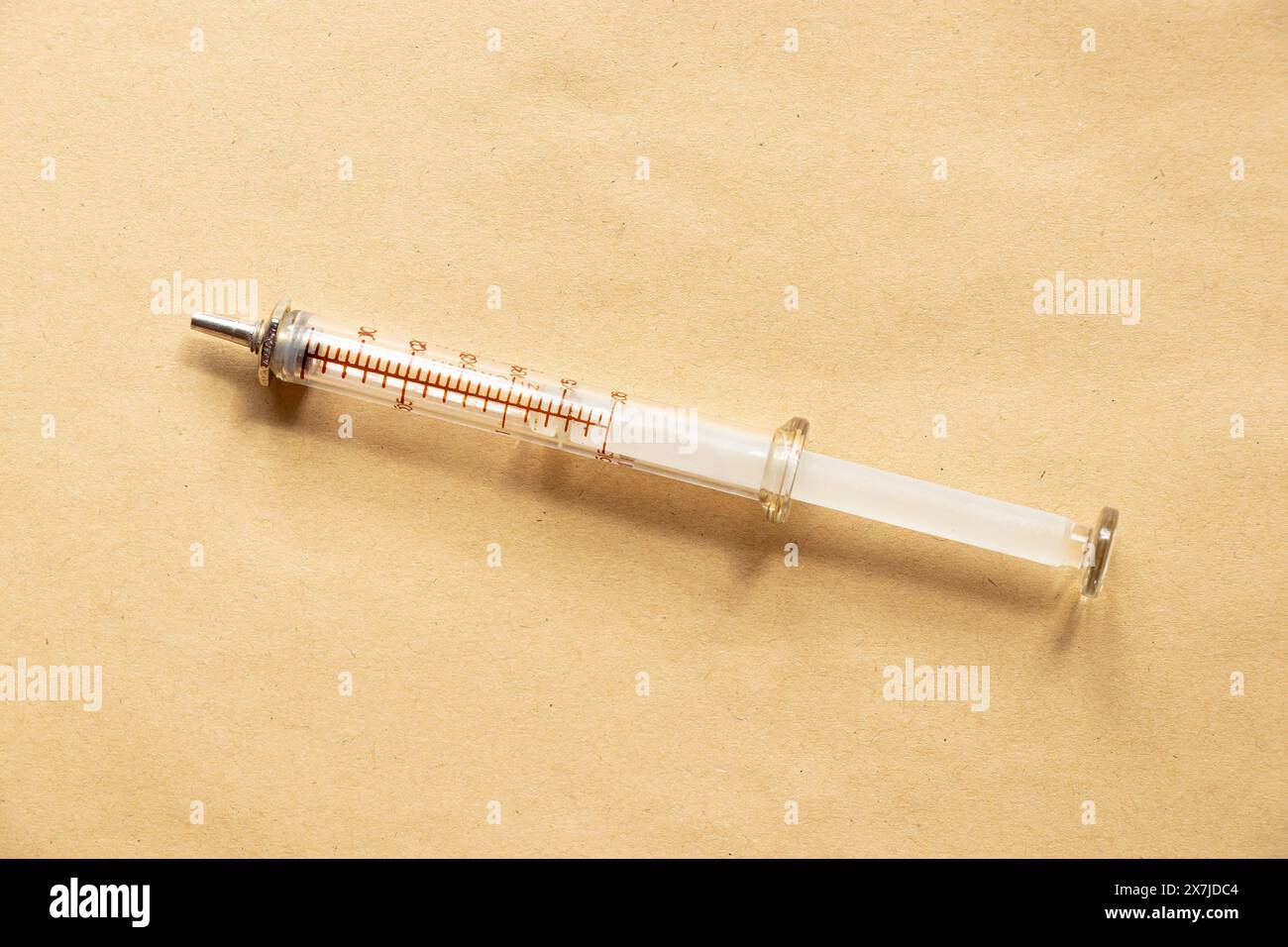 An old glass syringe lies on a brown background close-up Stock Photo
