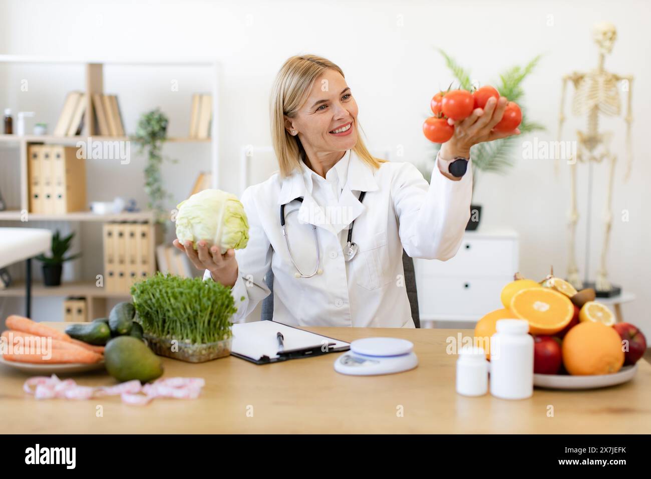 Caucasian woman makes diet of healthy food for treatment of gastritis. Mature female doctor nutritionist holds fresh organic tomatoes and cabbage in h Stock Photo