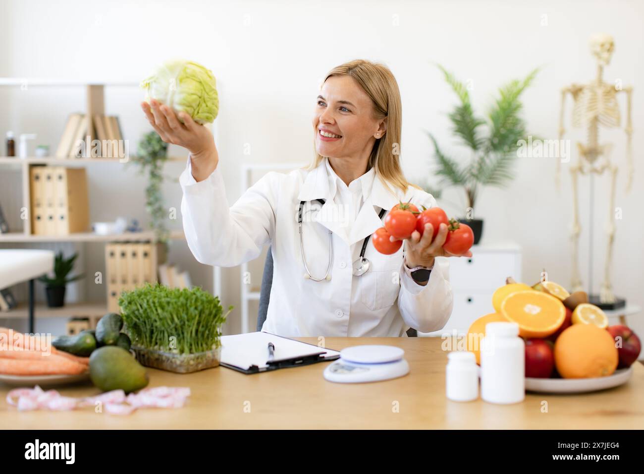 Caucasian woman makes diet of healthy food for treatment of gastritis. Mature female doctor nutritionist holds fresh organic tomatoes and cabbage in h Stock Photo