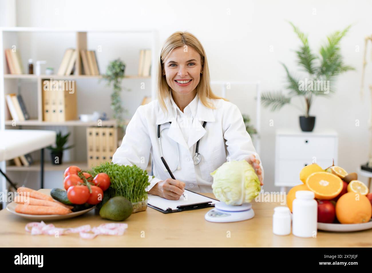 Concept of weight loss and treatment of gastrointestinal tract. Professional mature female nutritionist sitting at table in clinic and weighs cabbage, Stock Photo