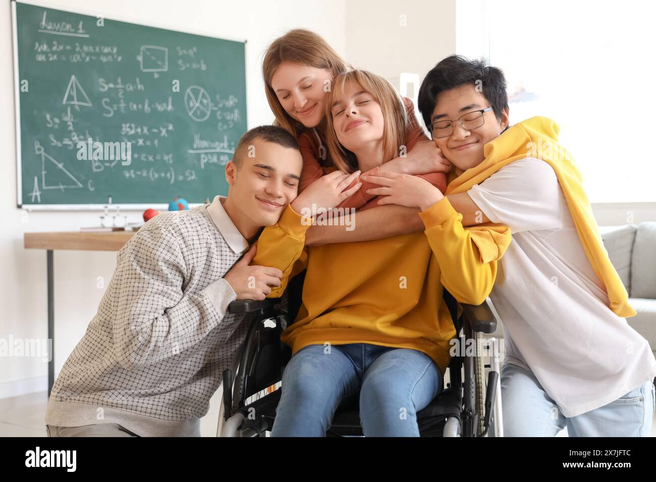 Group of teenage students with girl in wheelchair hugging at school ...