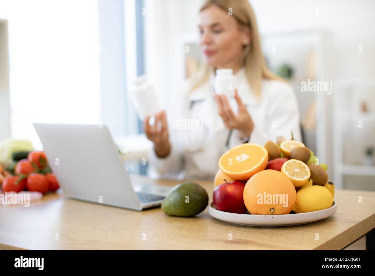 Caucasian doctor distantly describes the treatment plan. Positive mature nutritionist woman holding pills or vitamins in hands during online consultat Stock Photo