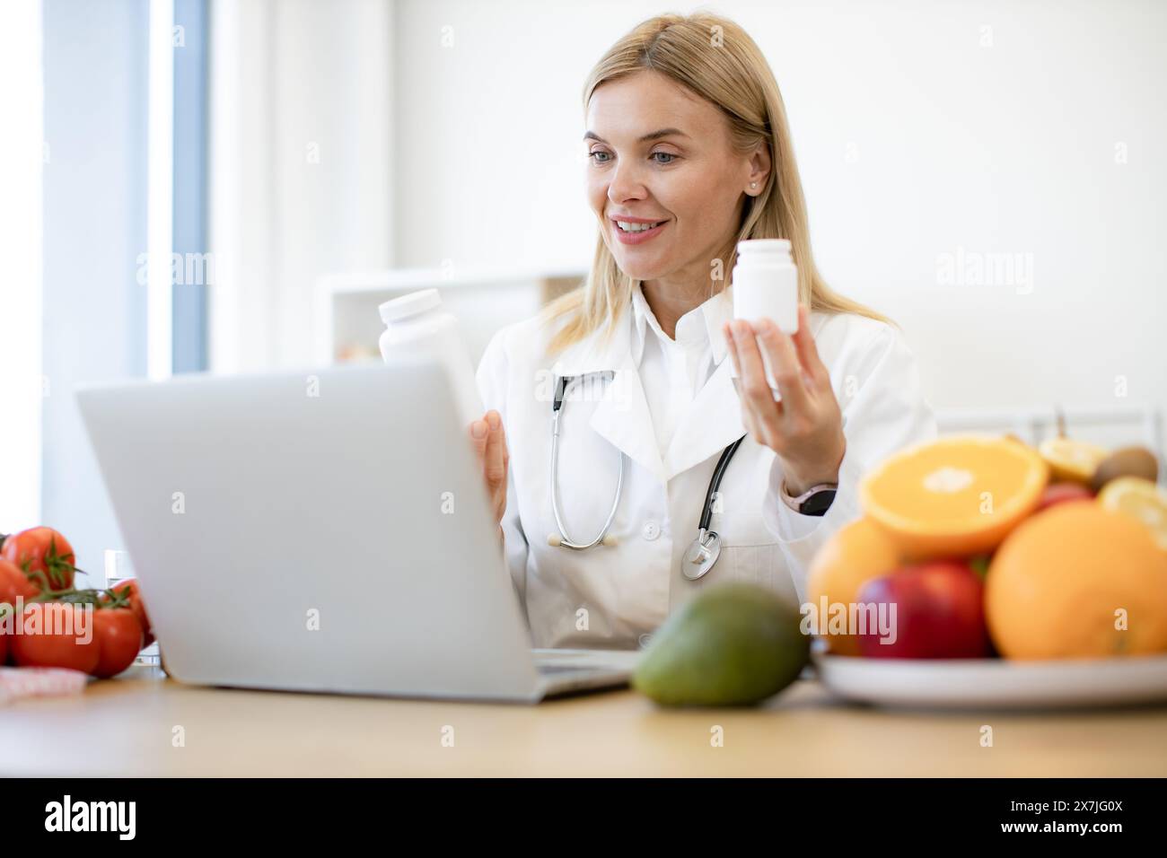 Caucasian doctor distantly describes the treatment plan. Positive mature nutritionist woman holding pills or vitamins in hands during online consultat Stock Photo
