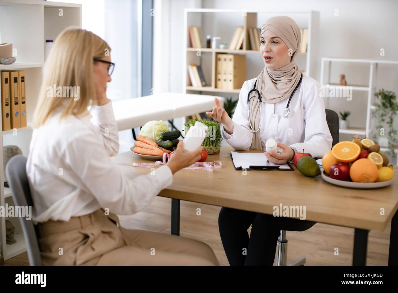 Muslim woman nutritionist makes plan for treatment of gastrointestinal tract using vitamins and supplements for healthy diet. Mature Caucasian lady re Stock Photo