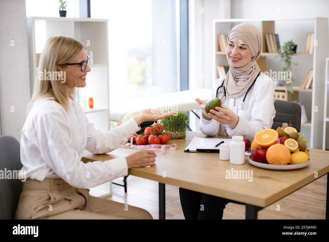 Professional nutritionist talks to patient about benefits of healthy diet while holding avocado. Arab female doctor makes treatment plan for gastroint Stock Photo