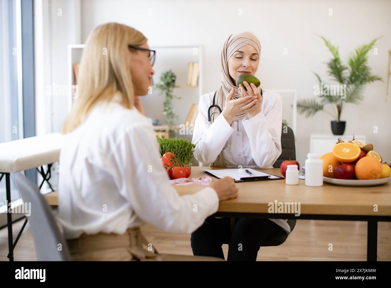Arab female doctor makes treatment plan for gastrointestinal tract while sitting at table in modern clinic. Professional nutritionist talks to patient Stock Photo