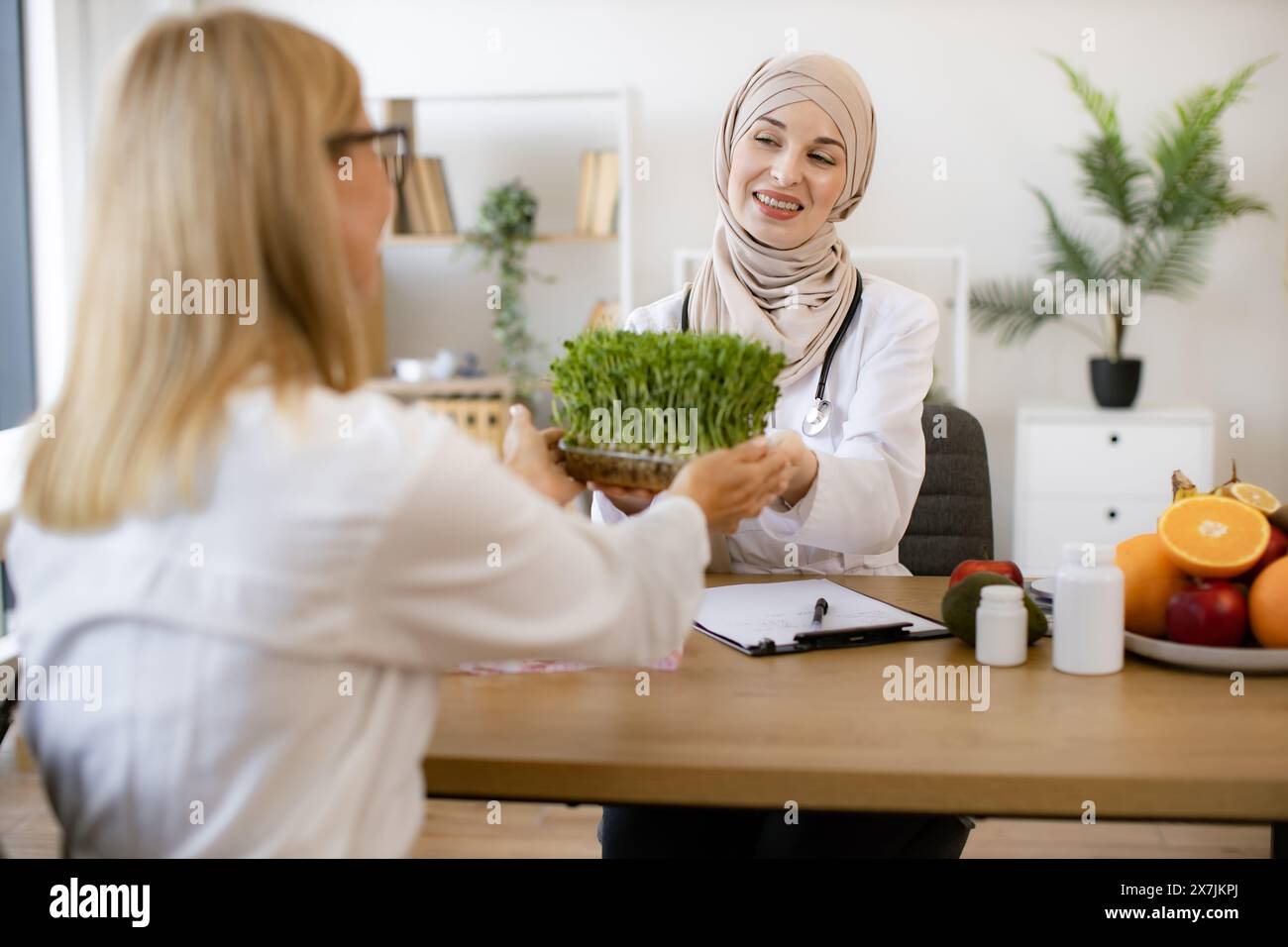 Arab female doctor makes treatment plan for gastrointestinal tract sitting at table in modern clinic. Professional nutritionist talks to patient about Stock Photo
