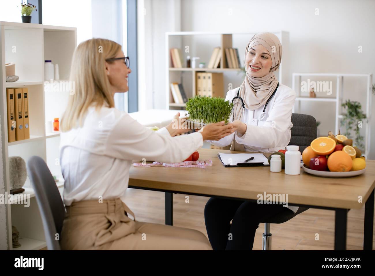 Professional nutritionist talks to patient about benefits of healthy diet while holding microgreen. Arab female doctor makes treatment plan for gastro Stock Photo
