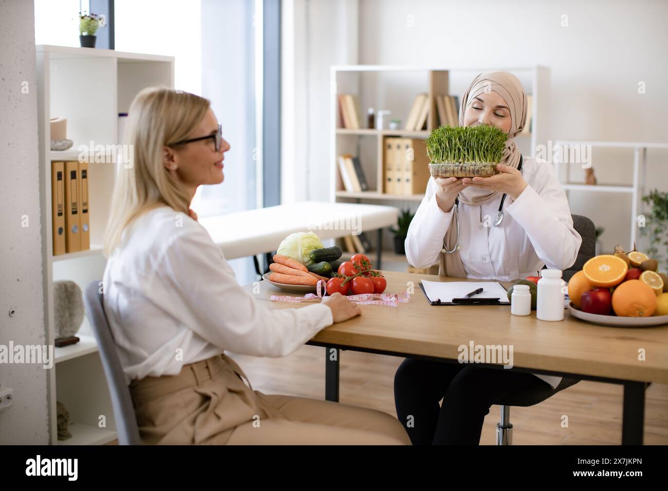Professional nutritionist talks to patient about benefits of healthy diet while holding microgreen. Arab female doctor makes treatment plan for gastro Stock Photo