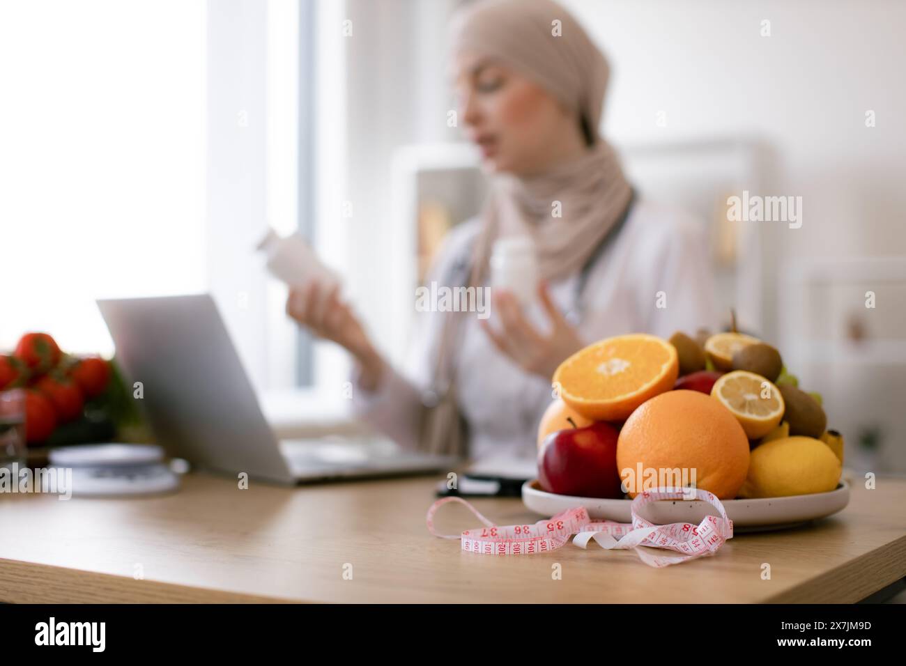 Close up on fruits with measuring tape. Muslim doctor distantly describes the treatment plan. Arabian nutritionist woman holding pills or vitamins in Stock Photo