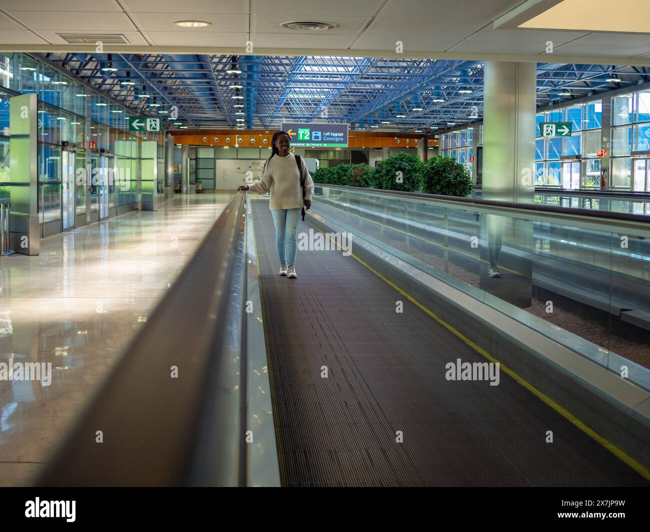 A young woman on a moving walkway inside an airport using her phone Stock Photo