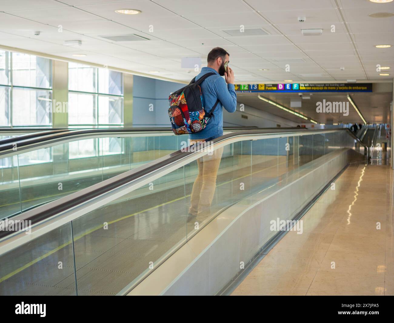 A young man on a moving walkway inside an airport using his phone Stock Photo