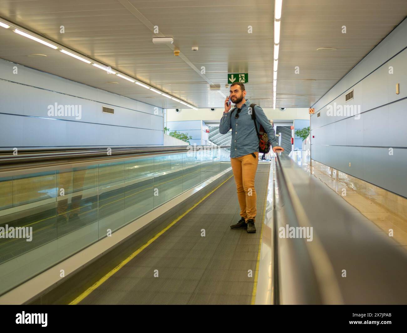 A young man on a moving walkway inside an airport using his phone Stock Photo