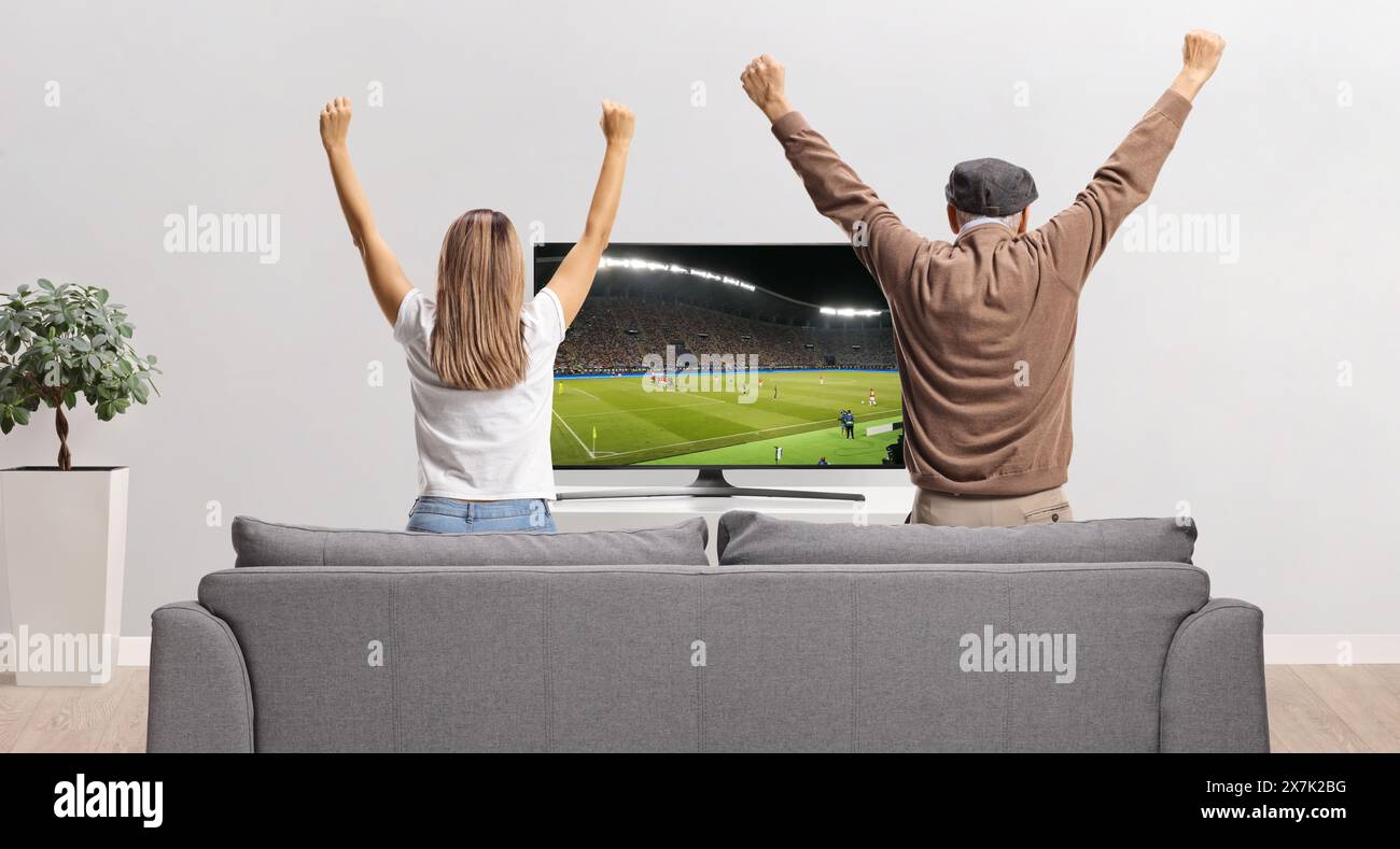 Rear view shot of an elderly man and a young woman watching a football match on tv at home Stock Photo