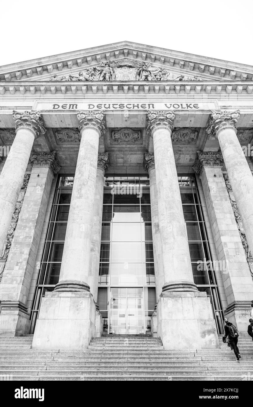 The monochrome facade of the Reichstag building, showcasing its iconic pillars and inscription: Dem Deutschen Volke. The seat of the German Bundestag, Berlin, Germany. Black and white image. Stock Photo