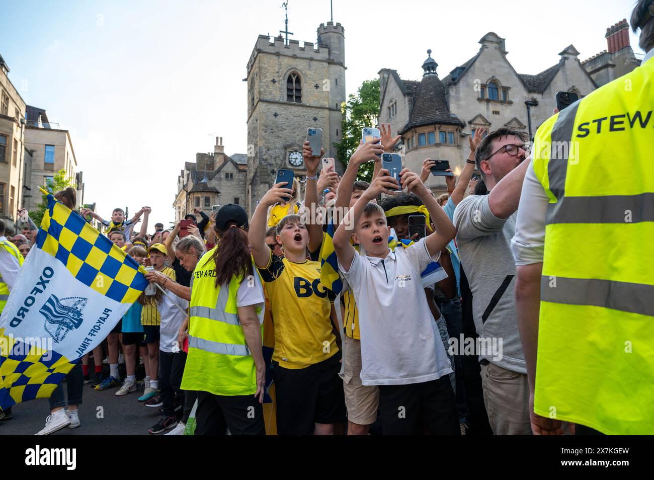 Thousands of Oxford United fans lined the city centre of Oxford to celebrate the promotion of Oxford United to the EFL Championship after beating the Bolton Wanders in the League One playoff at Wembley on the weekend. The crowds, decked out in yellow, cheered loudly and let off yellow flares as the open-top bus carrying the team and staff slowly moved along the High Street to the Oxford City Town Hall, where they attended an invite-only civic reception. The Oxford United flag flew over the Oxford City Council building in celebration. Stock Photo