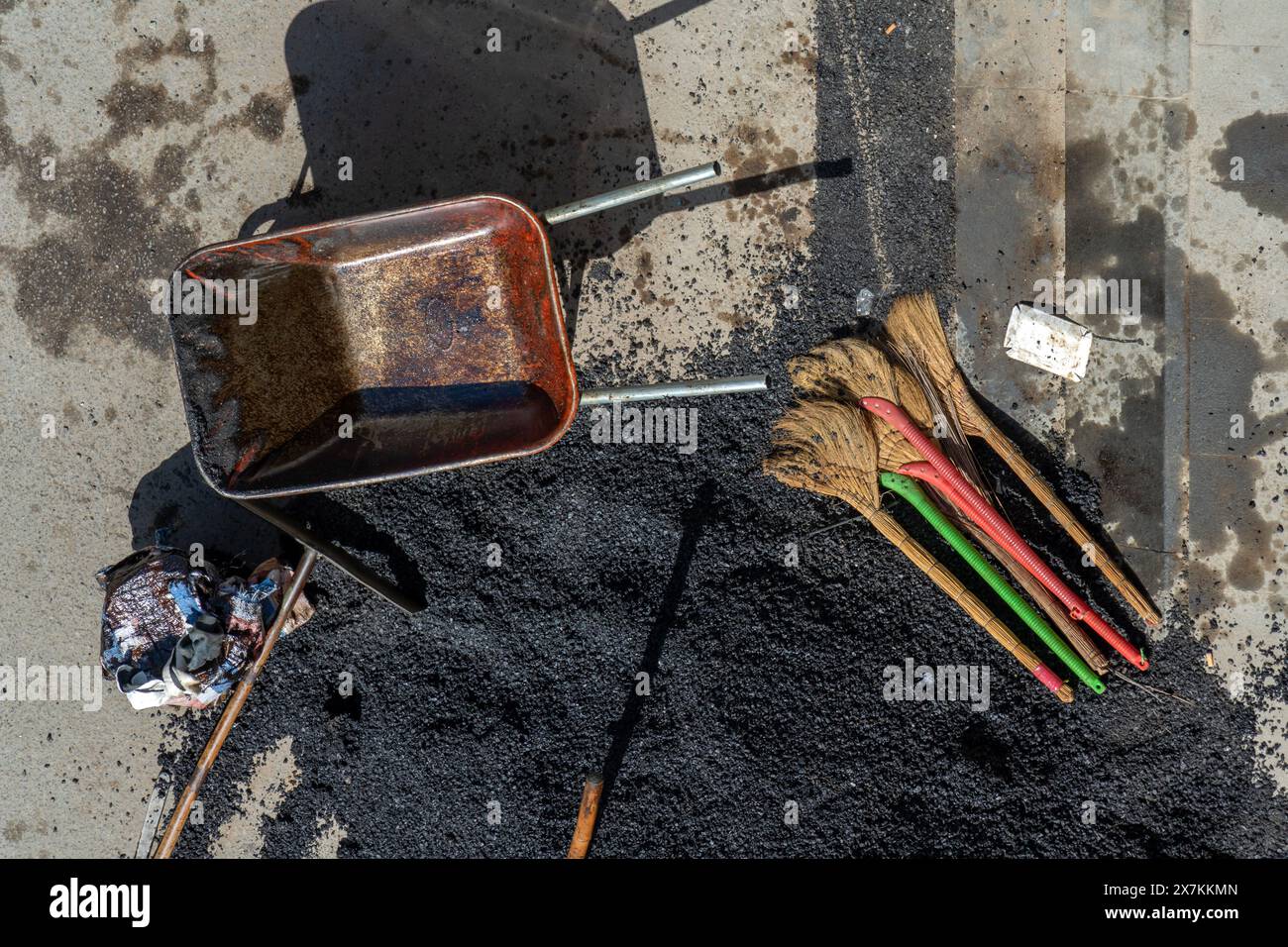 An empty wheelbarrow and tools near a pile of crushed asphalt lying on ...