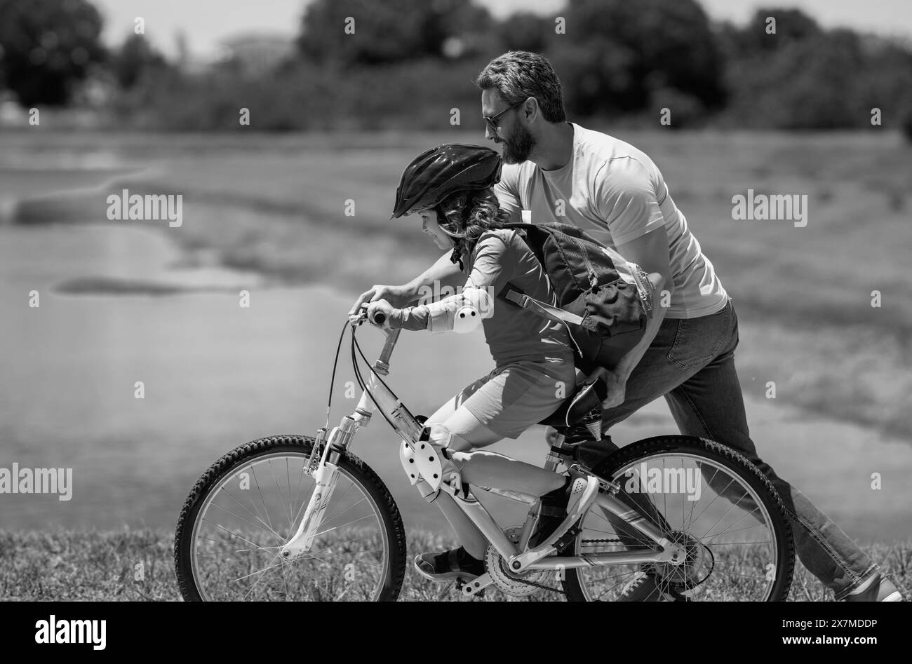 Happy Fathers day. Father and son in bike helmet for learning to ride bicycle at park. Father helping son cycling. Father and son on the bicycle on Stock Photo