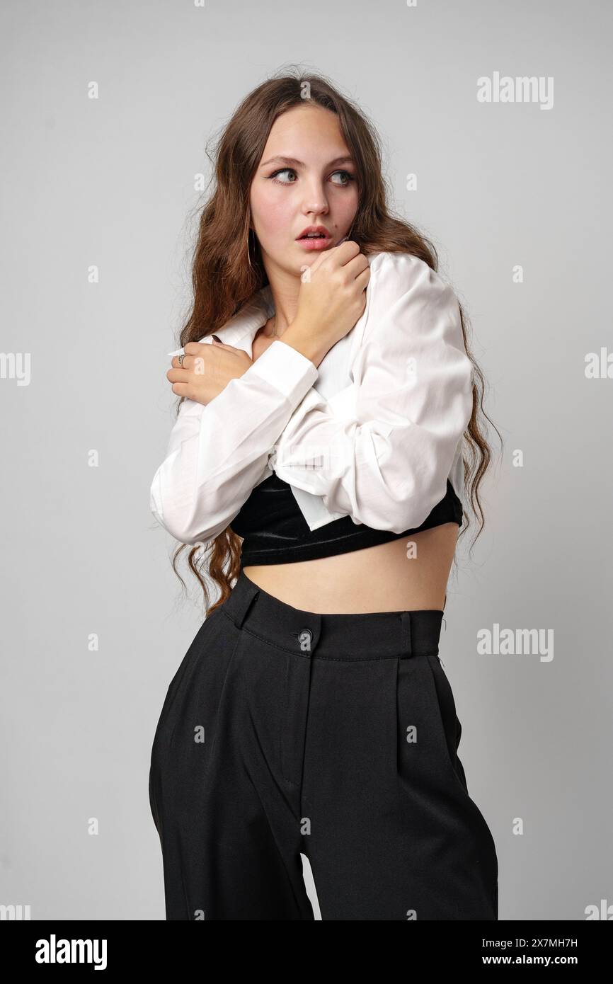Pensive Young Woman in White Shirt With Hand on Chin Against a Grey Background Stock Photo