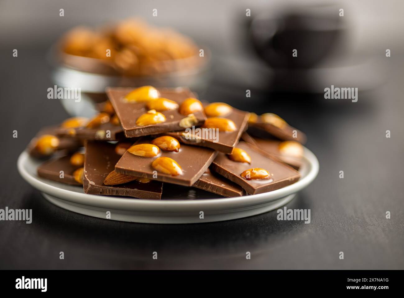 Broken chocolate bar with almonds on plate on a black table. Stock Photo