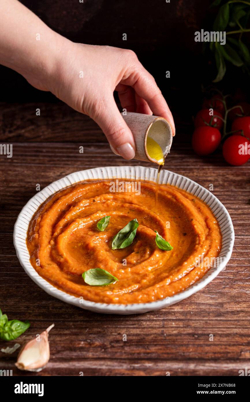 Hand pouring olive oil on fresh tomato sauce Stock Photo
