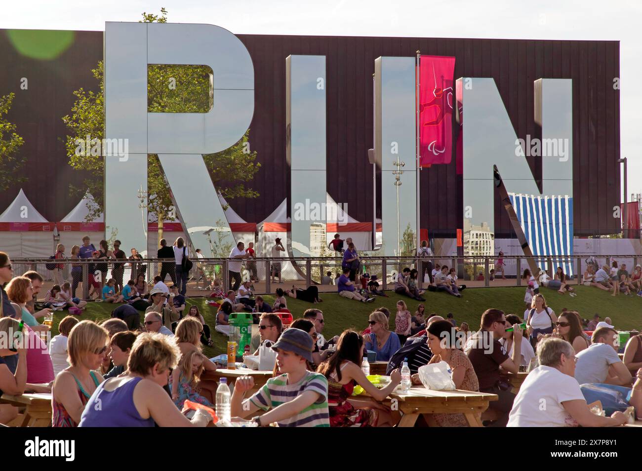 Spectators enjoying a picnic lunch, next to 'Run', a glass and stainless steel artwork outside the Copper Box, during the 2012 London Paralympics Stock Photo