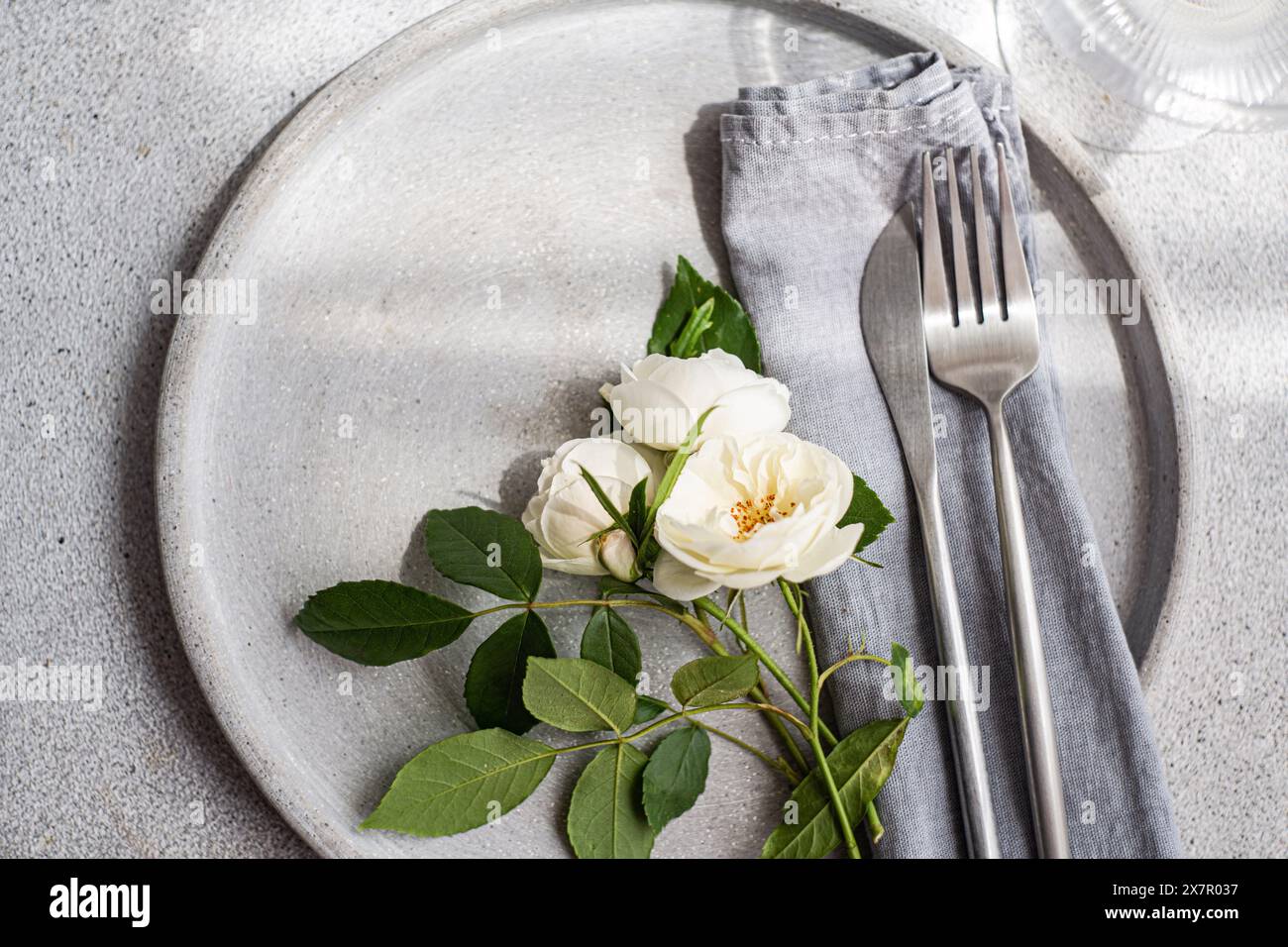 A sophisticated table setting featuring a neutral ceramic plate, silver ...