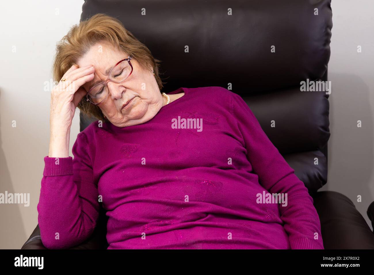 An elderly woman in a purple sweater looks fatigued and distressed ...