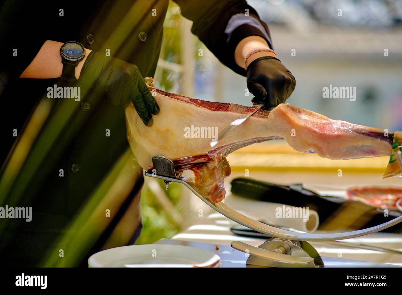 Cropped unrecognizable person in professional attire slicing thin pieces of , a Spanish cured ham, at a gourmet food stall. Stock Photo