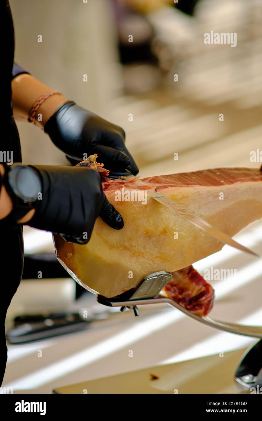 Cropped unrecognizable person expertly slices a premium ham leg at a gourmet buffet spread, showcasing culinary skills. Stock Photo