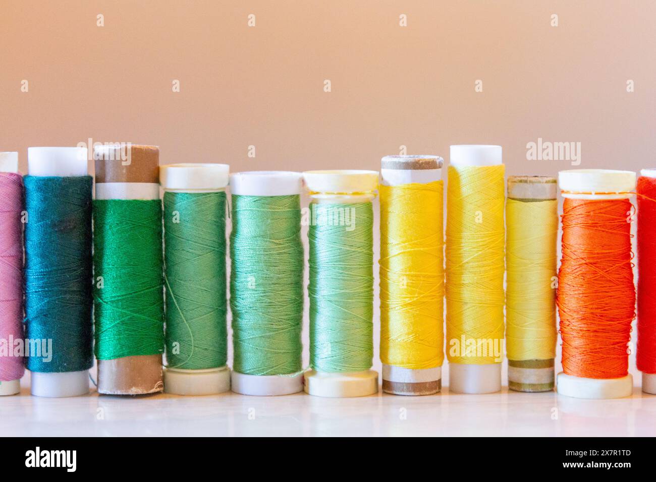 A vibrant array of colored sewing thread spools lined up on a table, showcasing materials for sewing and design Stock Photo