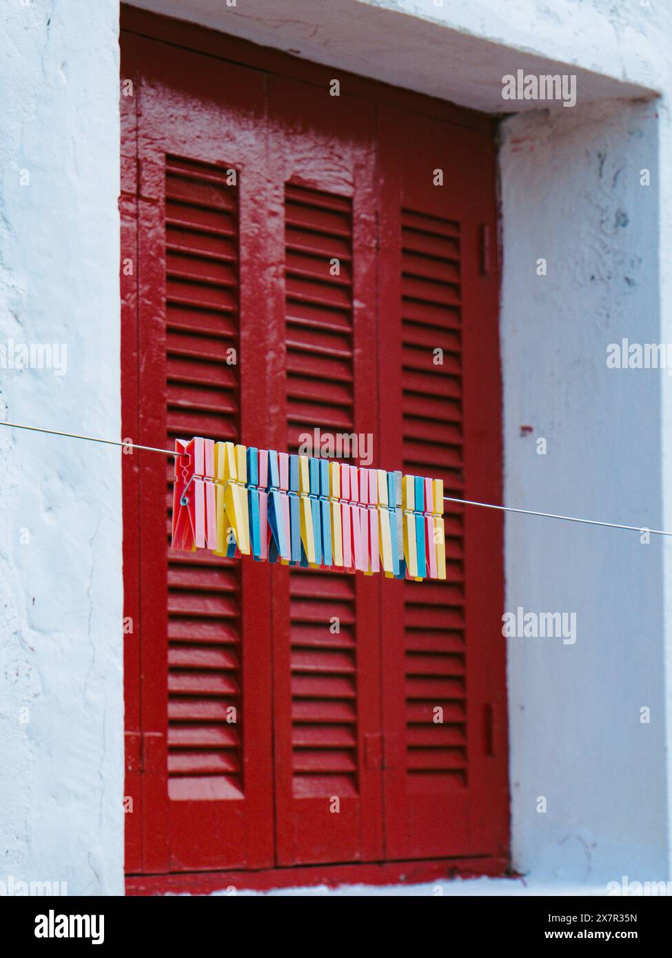 Colorful clothespins line up on a string against a rustic red door with ...