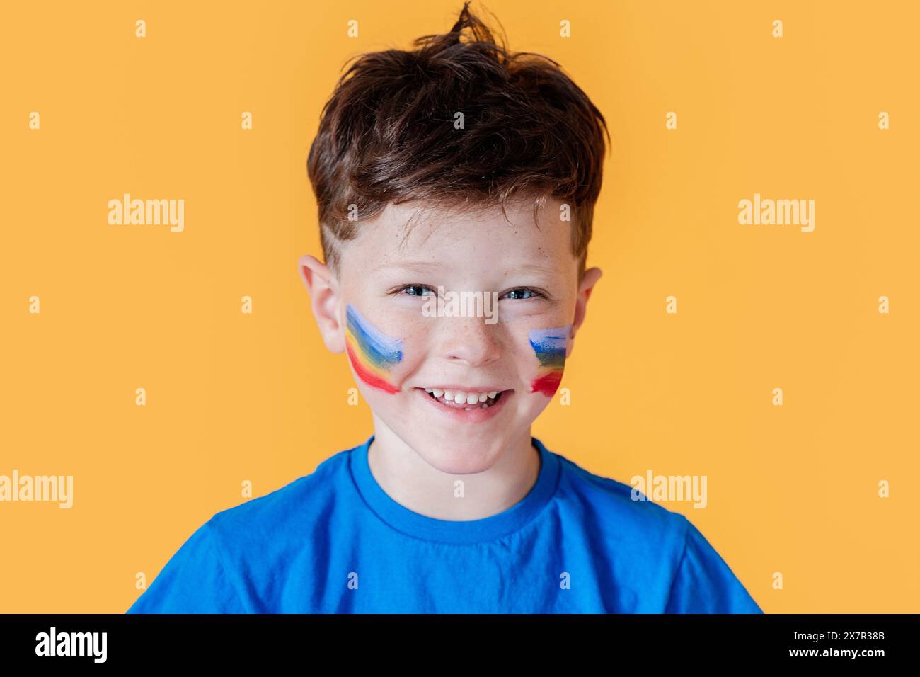 A young boy smiles broadly wearing a blue shirt and vibrant face paint ...