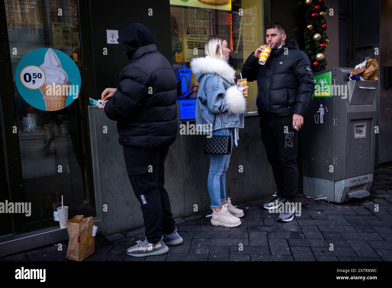 Tourists eat a fast food meal in front of a McDonalds restaurant in Dam Square in Amsterdam, capital of the Netherlands in Europe on 28 November 2021. Stock Photo