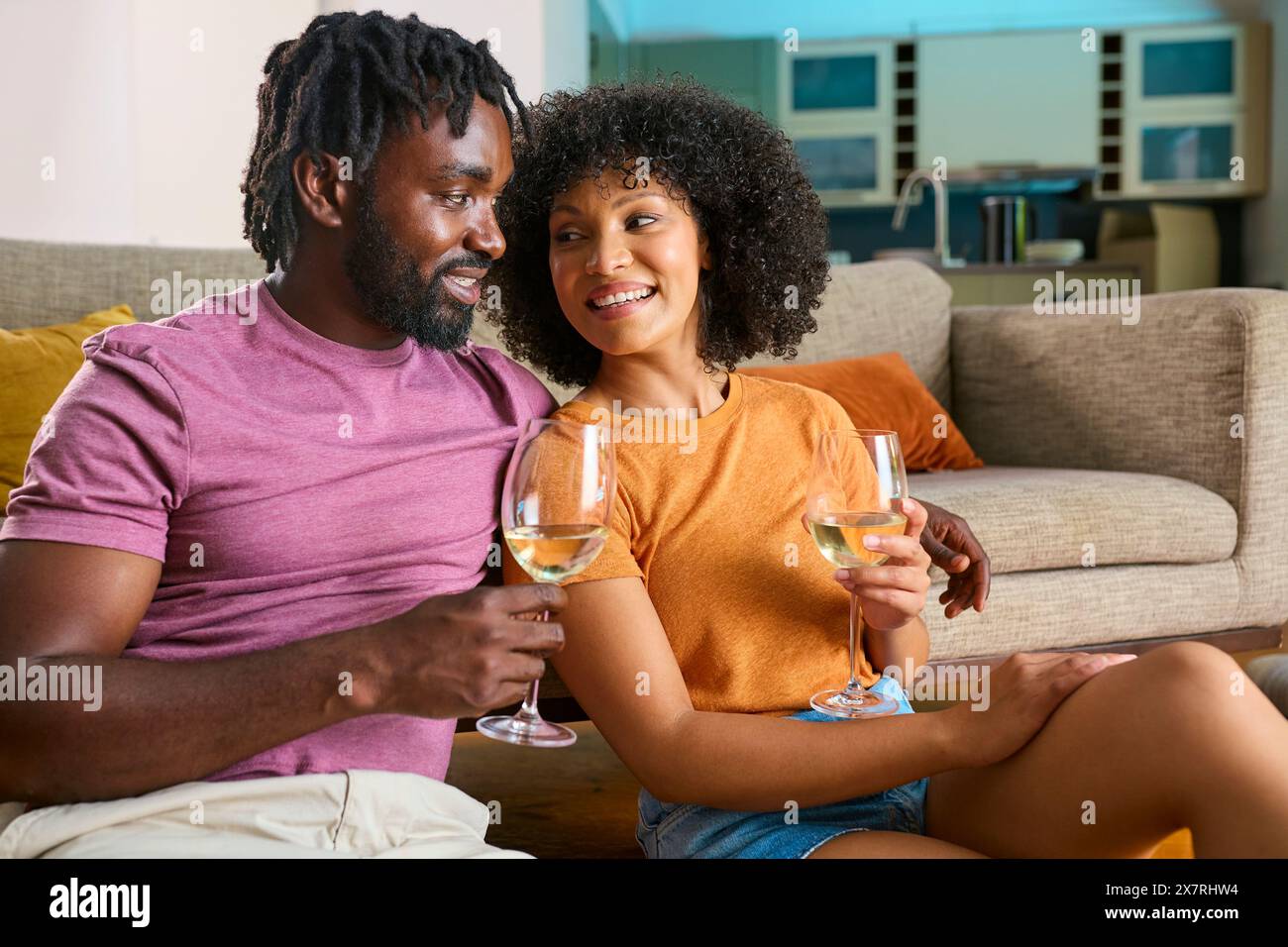 Young Couple Relaxing At Home Sitting On Floor Next To Sofa Drinking Wine Stock Photo