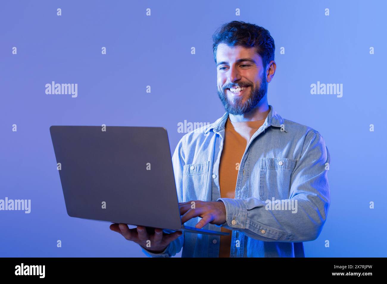 Man Smiles Using Laptop Computer in Neon Light Stock Photo