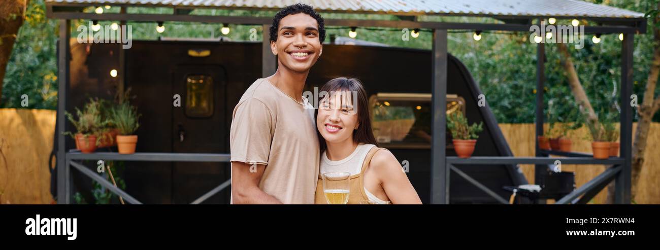 A man stands besides a woman, holding a glass of wine in a romantic moment during their interracial couple getaway. Stock Photo