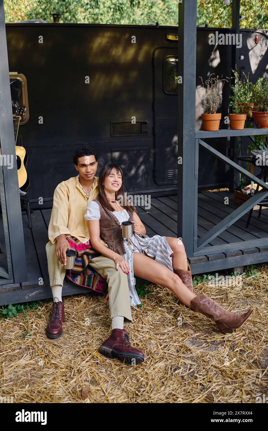 An interracial couple sitting close, enjoying a romantic moment in a camper van surrounded by the beauty of nature. Stock Photo