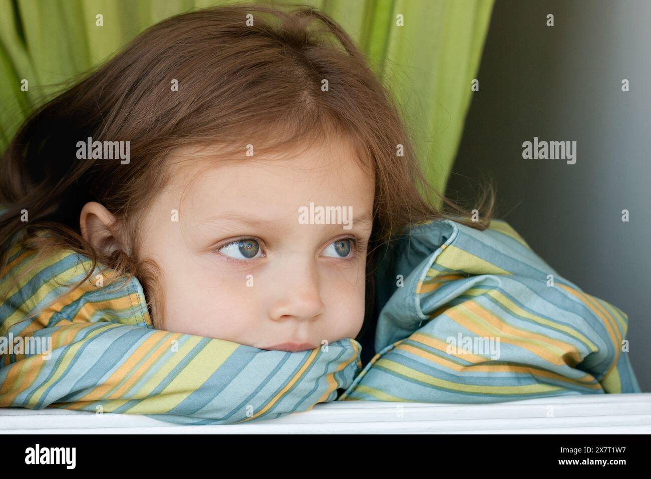 cute day dreaming little girl covered with blanket looking out the