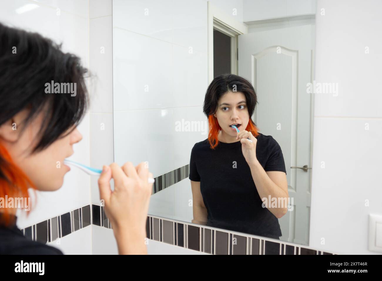 White person brushin their teeth while looking at themselves in the bathroom mirror Stock Photo