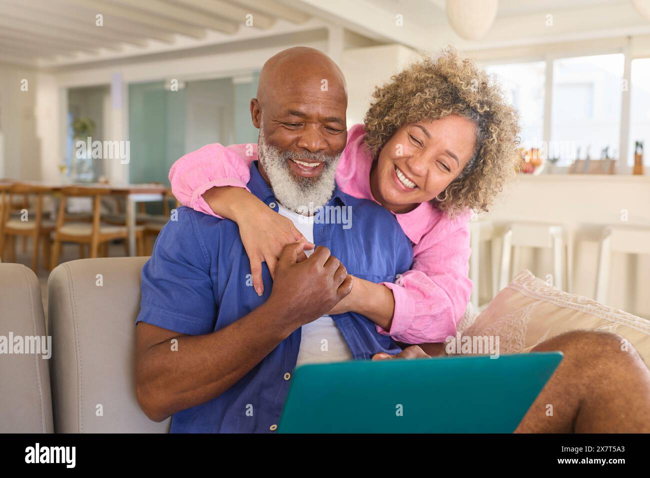 Mature Couple At Home With Woman Hugging And Surprising Man Using Laptop Sitting On Sofa Stock Photo