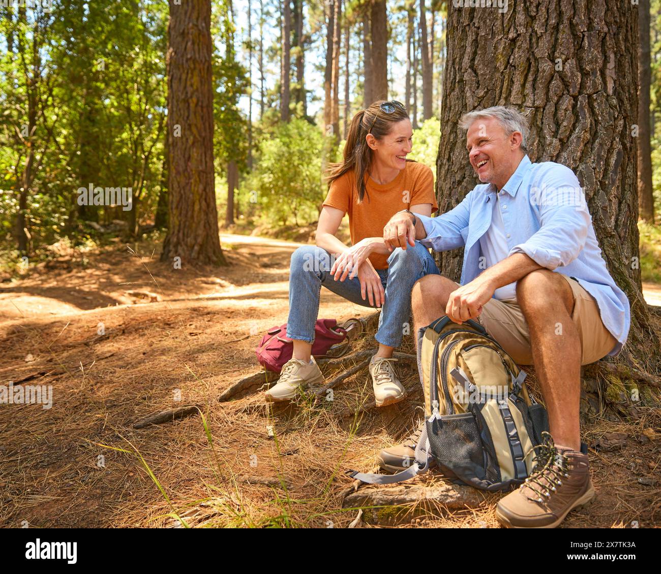 Retired Senior Couple Taking A Break Sitting At Base Of Tree On Hike Through Countryside Stock Photo