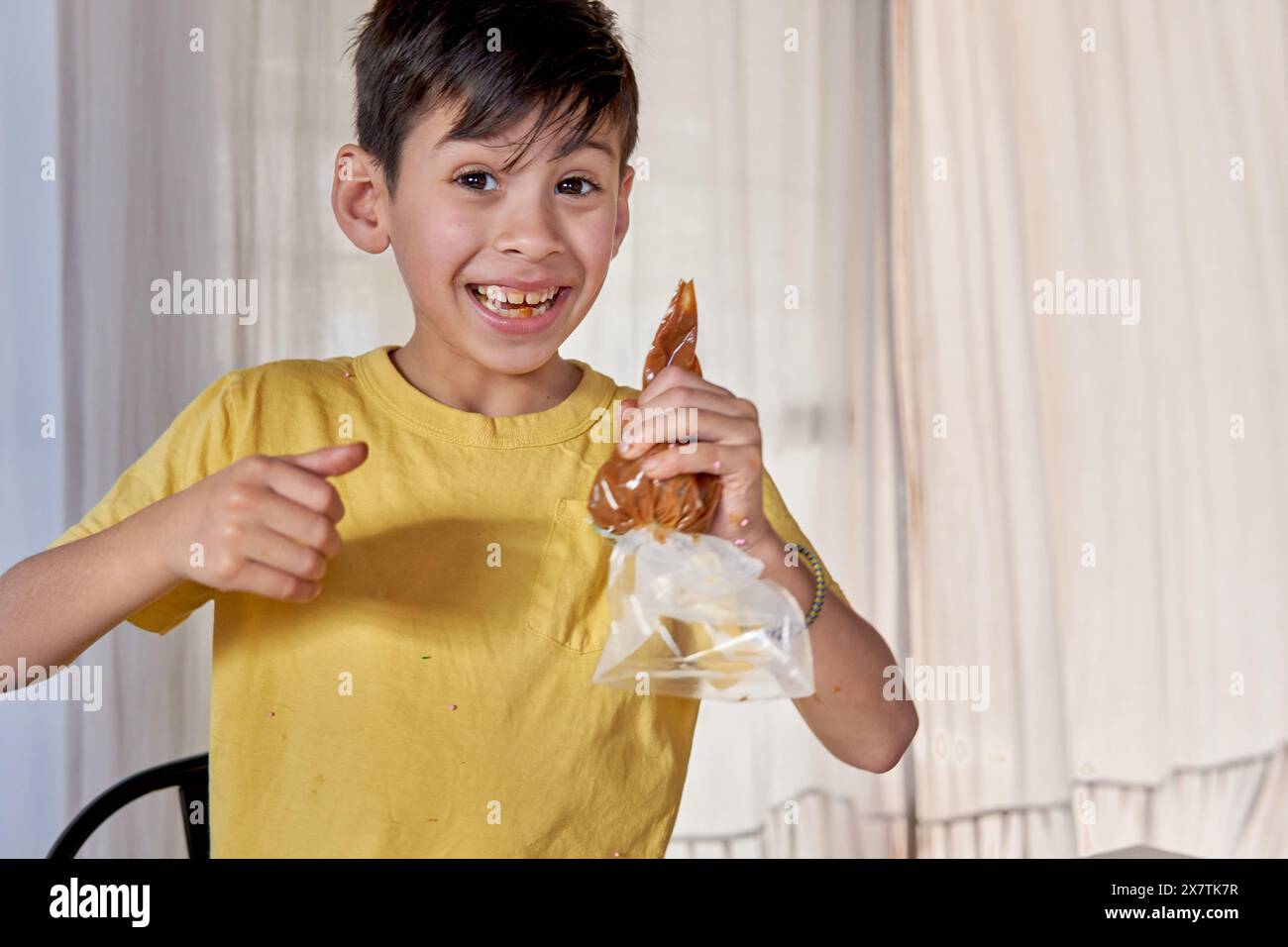 Latin boy smiling with a pastry bag with dulce de leche in one hand and making ok with the other. Concept of a little cook Stock Photo