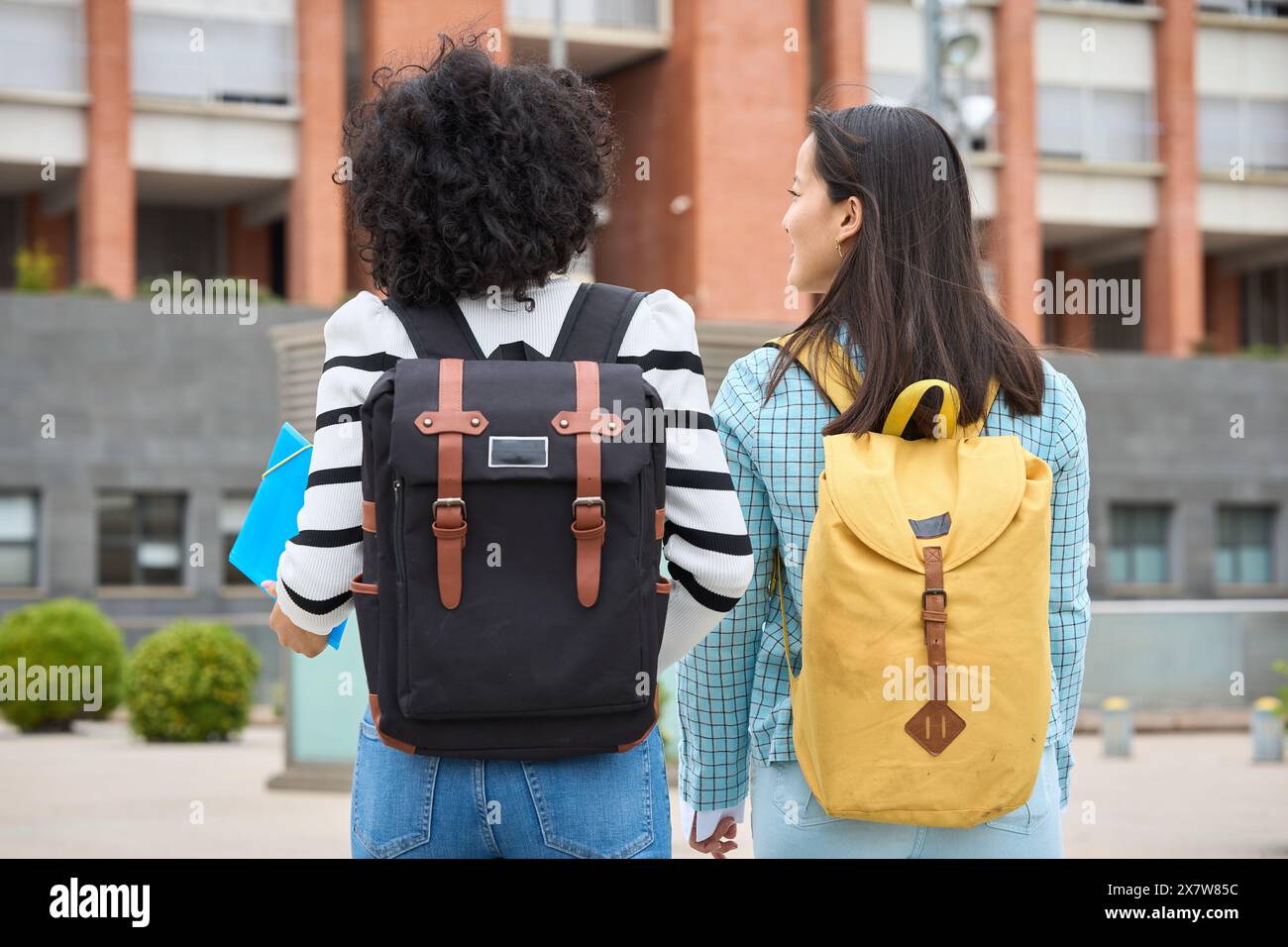 Two young students are walking down the street, each carrying a backpack Stock Photo