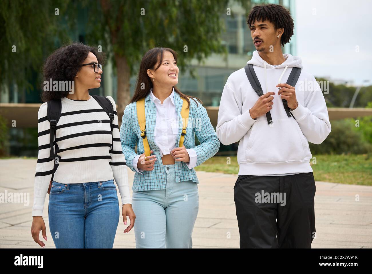 Three young students walking down a sidewalk outside the University Stock Photo