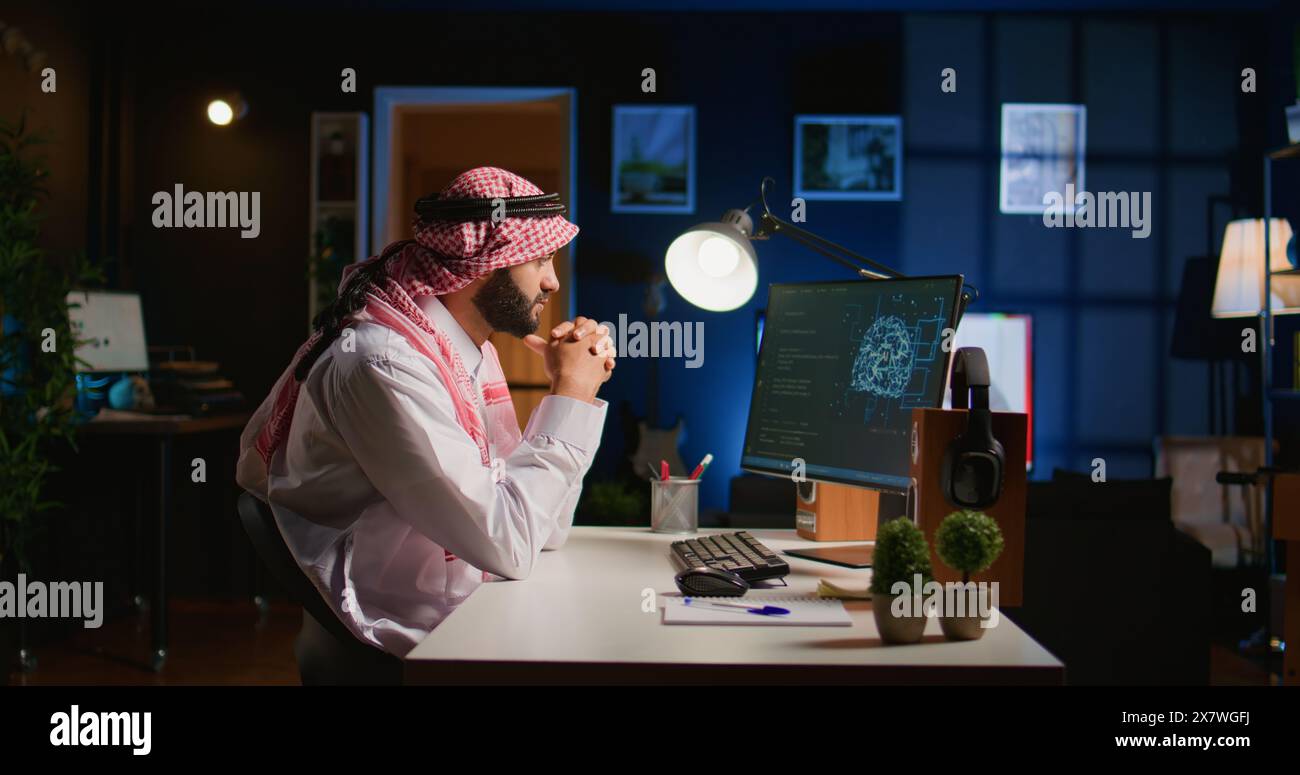 Licensed arabic engineer updating neural networks, writing intricate binary code scripts on computer. Middle Eastern man uses digital device programming to upgrade AI datasets at home Stock Photo