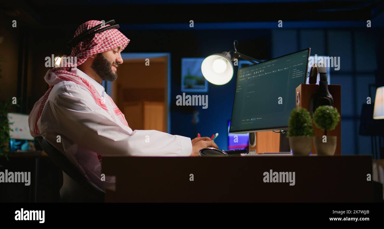 Smiling muslim engineer writing script code on computer screen using Java programming languages. Self employed Middle Eastern developer at home working on fixing database errors Stock Photo