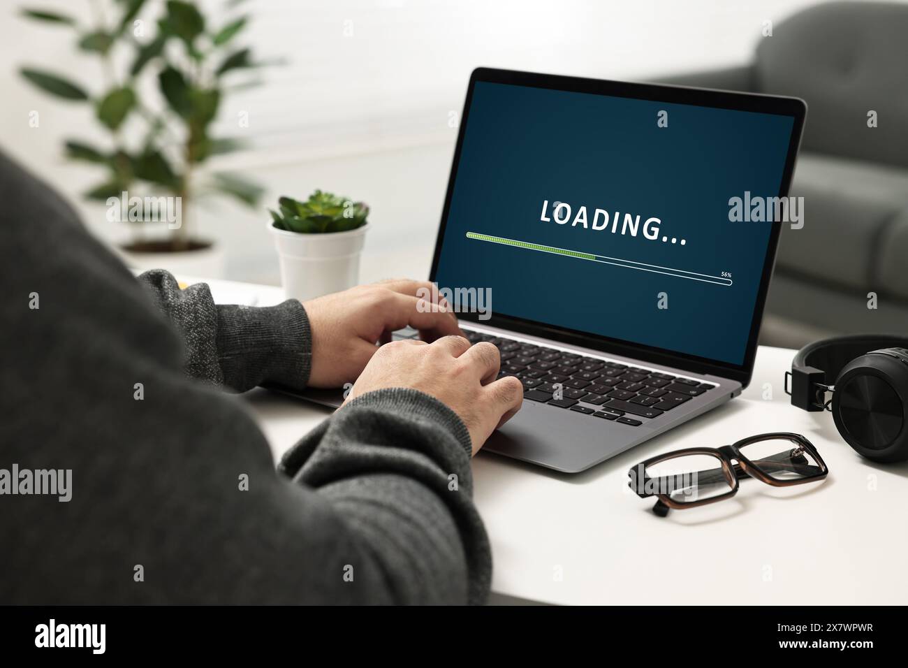Loading screen displaying progress. Man working on laptop at table indoors, closeup Stock Photo