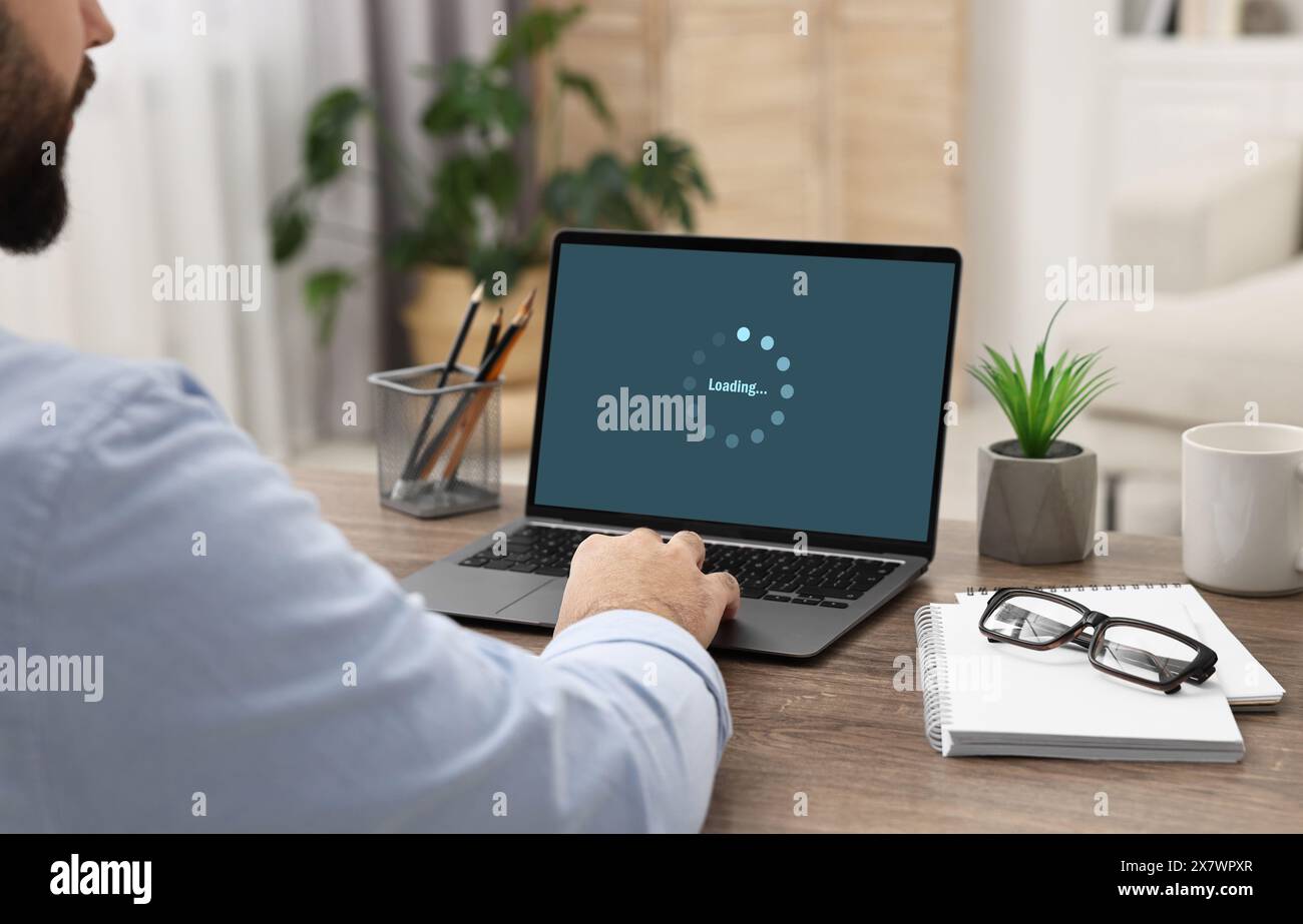 Loading screen displaying progress. Man working on laptop at table indoors, closeup Stock Photo